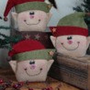 Peut inclure: Trois lutins de Noël en feutre faits à la main avec des chapeaux rouges et verts. Les lutins ont des visages blancs avec des yeux noirs et des sourires. Ils sont assis sur une surface en bois.