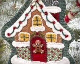 Peut inclure: Une décoration de Noël en forme de maison en pain d'épices en feutre avec une porte rouge, un bonhomme en pain d'épices et des garnitures vertes et rouges. La maison est décorée de glaçage blanc et de bonbons.
