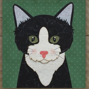 Op de afbeelding: Een grillige illustratie van een zwart-witte kat met groene ogen en een roze neus. De vacht van de kat is versierd met wervelende patronen, tegen een groene achtergrond met witte stippen. De oren van de kat hebben witte punten.