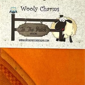May include: A rectangular piece of solid orange fabric attached to a white card header. The header features the text Wooly Charms, an illustration of a sheep, and a sign reading In The Patch DESIGNS with the website WWW.INTHEPATCHDESIGNS.COM.
