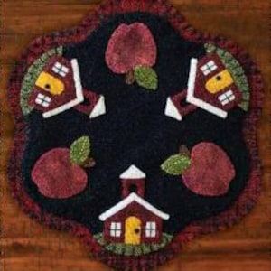 May include: A round, black wool rug with a scalloped edge. The rug features a repeating pattern of red schoolhouses and red apples with green leaves.