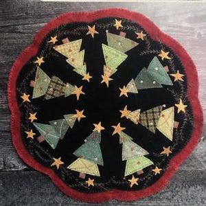 Puede incluir: Un cubremesa redondo de fieltro negro para árbol de Navidad con un borde rojo festoneado. El cubremesa presenta un círculo de árboles de Navidad de fieltro verde con troncos marrones y nieve de fieltro blanco. Hay estrellas de fieltro doradas esparcidas alrededor de los árboles.
