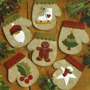 May include: Seven felt Christmas ornaments shaped like mittens, each with a different festive design: a gingerbread man, a Christmas tree, a snowman, a holly sprig, a Santa Claus, an ice skate, and a star.