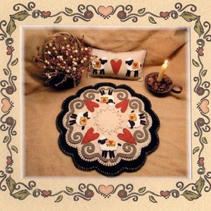 May include: A wool felt rug with a scalloped edge and a design of sheep and hearts. The rug is surrounded by a decorative border of hearts and vines.