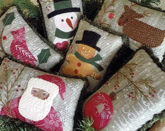 May include: A collection of six handmade Christmas pillows featuring various holiday themes. The pillows are made of a gray fabric with embroidered designs, including a snowman, gingerbread man, cardinal, reindeer, Santa Claus, and a Christmas ornament.