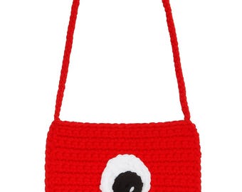 May include: A red crocheted shoulder bag with a white and black eye design. The bag has a rectangular shape and a long, red strap. The bag is made of a thick, textured yarn.