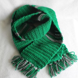 May include: A handmade green and gray crochet scarf with fringe. The scarf is a vibrant green with gray stripes and fringe at the ends. The scarf is made of soft yarn and is perfect for keeping warm during the colder months.