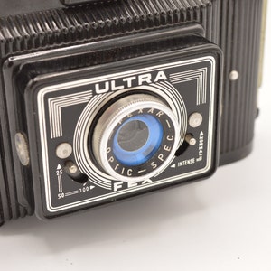 May include: A black vintage camera with a silver lens and the word "ULTRA" printed on the front. The camera has a dial for adjusting the aperture and a dial for adjusting the shutter speed.