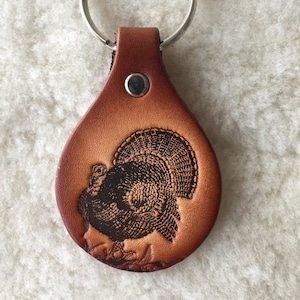 May include: A brown leather keychain with a detailed engraved image of a turkey.