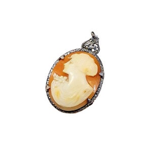 May include: A cameo pendant featuring a woman's profile carved in shell, set in a silver frame with a filigree design.