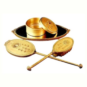 May include: A gold-toned vanity set with a round mirror, a brush, and a hand mirror. The set has an ornate design with floral motifs.