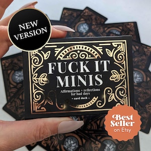 May include: A black card deck box with gold foil filigree borders and the white text FUCK IT MINIS, followed by the subtitle Affirmations + reflections for bad days, card deck. A black circular sticker reads NEW VERSION and an orange sticker reads Best Seller on Etsy.