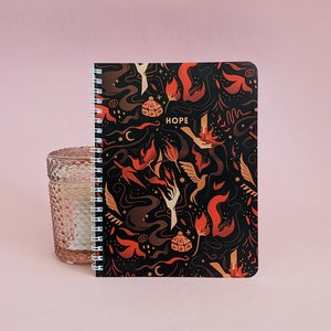 May include: A black spiral bound notebook with a colorful design featuring flames, swirls, and the word "HOPE".