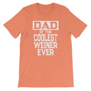 May include: Orange short-sleeved t-shirt with white text that reads "DAD OF THE COOLEST WEINER EVER".
