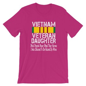 May include: Pink t-shirt with a white graphic that says "VIETNAM VETERAN DAUGHTER" with a yellow and green ribbon. The text below the graphic says "Most People Never Meet Their Heroes I Was Blessed To Be Raised By Mine."