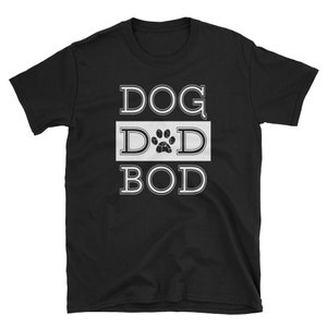 Op de afbeelding: Zwart T-shirt met de tekst "DOG DAD BOD" in witte blokletters. Het woord "DAD" heeft een pootafdruk in plaats van de "A". Het shirt is een T-shirt met korte mouwen en een ronde hals.