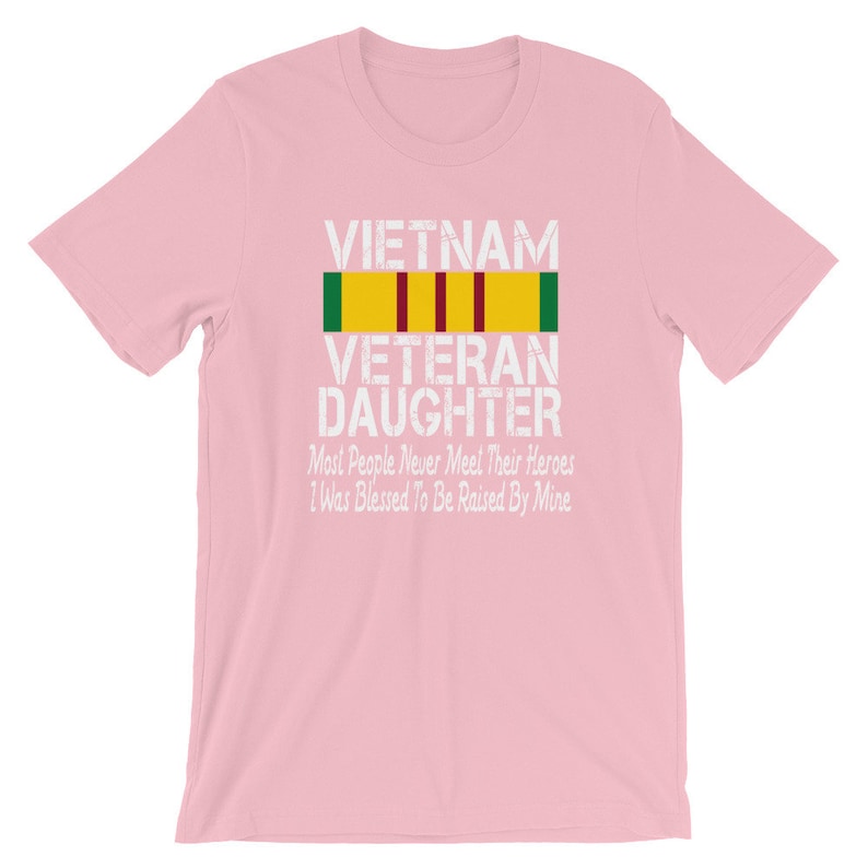 May include: Pink t-shirt with a white graphic that says "VIETNAM VETERAN DAUGHTER" with a yellow, red, and green ribbon above the text. The graphic also says "Most People Never Meet Their Heroes I Was Blessed To Be Raised By Mine".