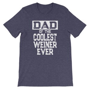 May include: A heather blue t-shirt with a white graphic that reads "DAD OF THE COOLEST WEINER EVER".