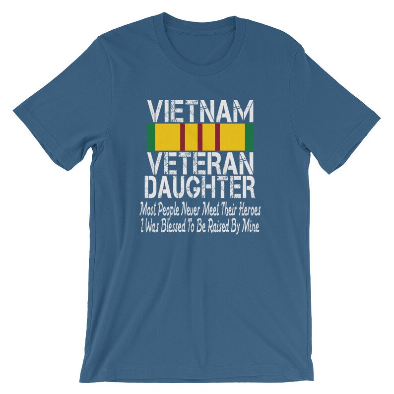 May include: A blue t-shirt with a white distressed graphic that reads "VIETNAM VETERAN DAUGHTER" with a green, yellow, and red ribbon above the text. The text below the ribbon reads "Most People Never Meet Their Heroes I Was Blessed To Be Raised By Mine."