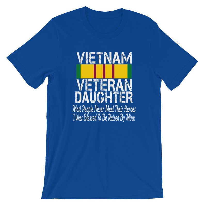 May include: Blue t-shirt with a white graphic that says "VIETNAM VETERAN DAUGHTER" with a yellow and green ribbon above the text. The text below the ribbon says "Most People Never Meet Their Heroes I Was Blessed To Be Raised By Mine".