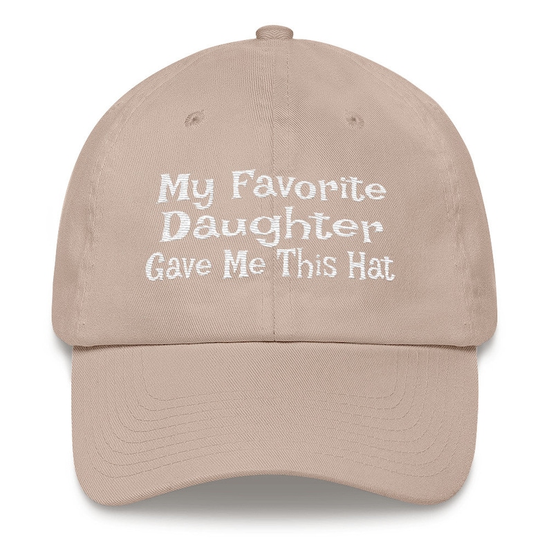 May include: A beige baseball cap with white embroidered text that reads "My Favourite Daughter Gave Me This Hat".