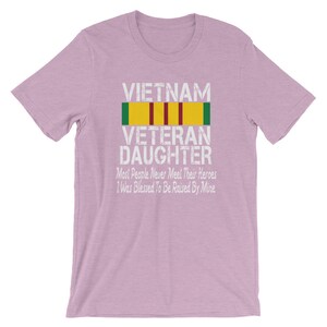 May include: A light purple t-shirt with the text "VIETNAM VETERAN DAUGHTER" and a military ribbon. The text below the ribbon reads "Most People Never Meet Their Heroes I Was Blessed To Be Raised By Mine."