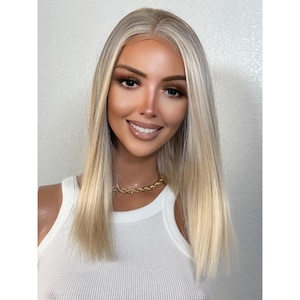 Könnte beinhalten: Eine lange, glatte, blonde Perücke mit einem hellbraunen Ansatz. Die Perücke ist mit einem Mittelscheitel gestylt und hat einen natürlichen, fließenden Look.