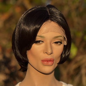 May include: A mannequin head with a short, black wig styled in a bob cut. The wig features a natural-looking hairline and is styled with a side part. The mannequin is wearing a white tank top.