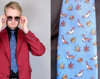 May include: A red blazer, black shirt, and blue tie. The tie has a pattern of ducks and leaves. The blazer has a two-button closure and a notched lapel. The person is wearing round sunglasses.