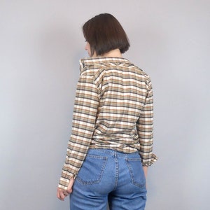 May include: A brown and white checked long-sleeved shirt with a collared neckline. The shirt is worn with blue jeans.