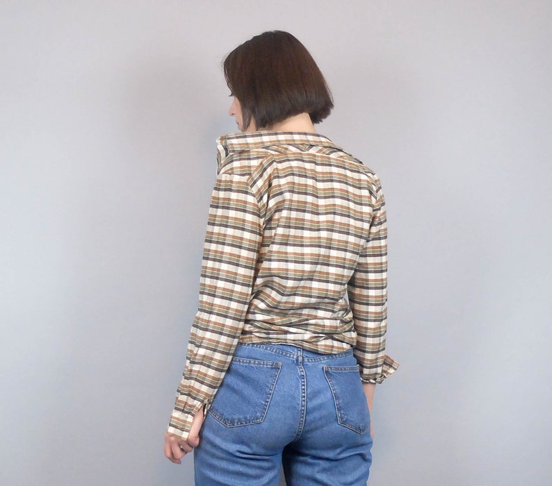 May include: A brown and white checked long-sleeved shirt with a collared neckline. The shirt is worn with blue jeans.
