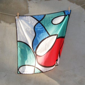 Puede incluir: Un dise&ntilde;o abstracto colorido en una tela blanca con formas rojas, azules, verdes y blancas. La tela est&aacute; colgada de un tendedero.