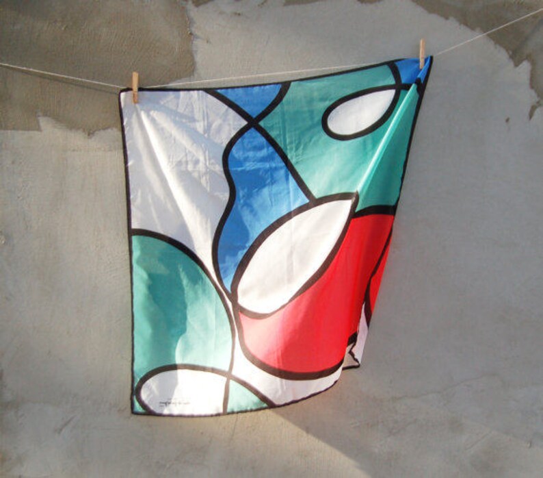 Puede incluir: Un dise&ntilde;o abstracto colorido en una tela blanca con formas rojas, azules, verdes y blancas. La tela est&aacute; colgada de un tendedero.
