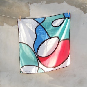 Puede incluir: Una bufanda de seda blanca con un dise&ntilde;o abstracto colorido. El dise&ntilde;o presenta formas grandes y redondeadas en tonos de azul, verde, rojo y blanco.