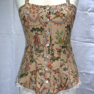 May include: A beige corset with a floral and patterned design. The corset has white lace trim and is fastened with buttons down the front.