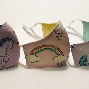 May include: Three pink fabric face masks with white straps. The masks feature different unicorn and rainbow designs. One mask has a purple unicorn, one has a blue unicorn, and one has a rainbow with clouds.