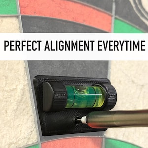 May include: A black leveler with a green bubble is mounted on a dartboard. The leveler is used to ensure that the dartboard is perfectly aligned. The text "PERFECT ALIGNMENT EVERYTIME" is displayed above the leveler.