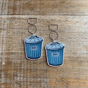 May include: Two blue and white trash can keychains with silver rings. Each keychain has the word "men" written on it.