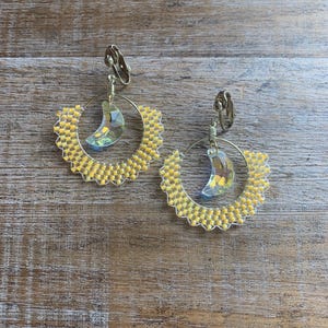 May include: A pair of yellow beaded hoop earrings with a crescent moon crystal charm hanging from each hoop.
