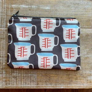 May include: A black zippered pouch with a repeating pattern of white measuring cups with red markings on a black background.