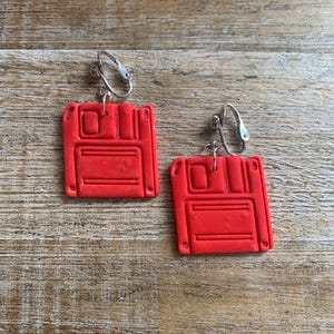 Peut inclure: Une paire de boucles d'oreilles en forme de disquette rouge avec des fermoirs clips argentés. Les boucles d'oreilles sont en pâte polymère et ont la forme d'une disquette classique de 3,5 pouces.