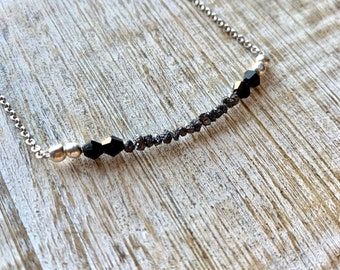 May include: A silver chain necklace with black beads and silver beads. The necklace is on a wooden surface.