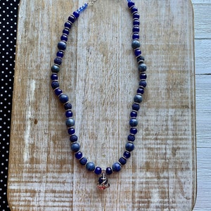 May include: A blue and silver necklace with a small anchor charm. The necklace is made with blue lava rock and blue glass beads.