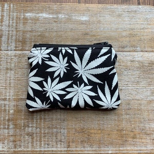 May include: A small black zippered pouch with a white marijuana leaf pattern.