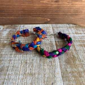 May include: Two colorful braided bracelets made from fabric scraps. The bracelets are connected by a silver chain.