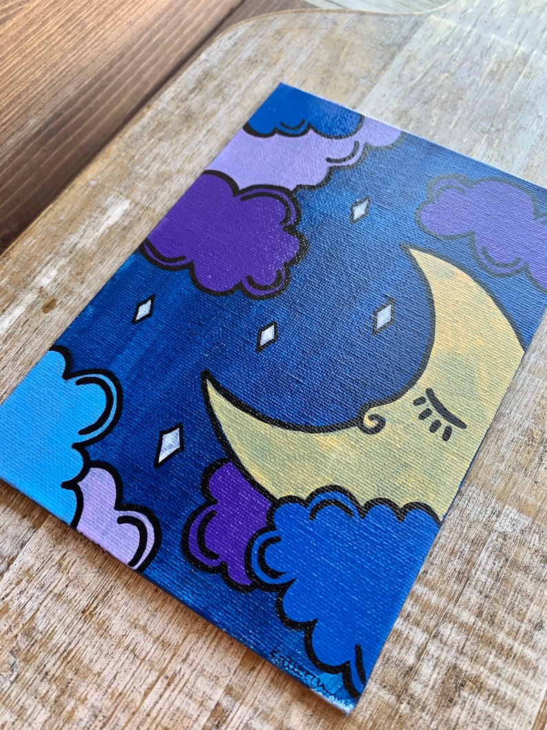 May include: A hand-painted canvas with a crescent moon and clouds in shades of blue, purple, and yellow. The moon has a face with closed eyes and a small smile.