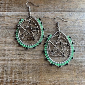 May include: A pair of dangle earrings with a silver pentagram charm inside a beaded hoop. The hoop is made of green and black beads.
