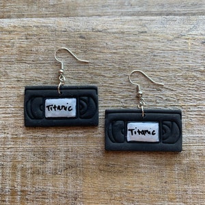May include: A pair of black and silver earrings shaped like VHS tapes with the word "Titanic" written on them.