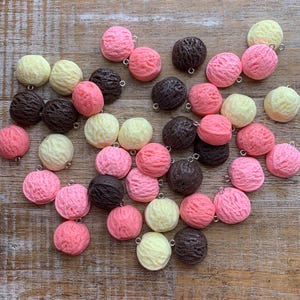 以下が含まれることがあります： カラフルなアイスクリームコーンチャーム25個のセット。チャームはプラスチック製で、表面にテクスチャがあります。ピンク、白、茶色の3色展開です。