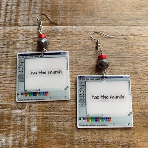 Può includere: Orecchini con un design a interfaccia computer e la scritta "tax the church". Ogni orecchino ha un gancio argentato, una perla rossa, una perla sfaccettata grigia e un ciondolo quadrato con una barra degli strumenti colorata.
